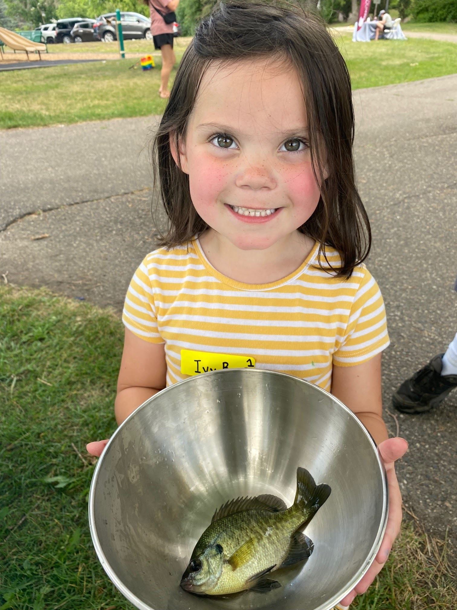 Small child holds a bowl with fish inside, posing and smiling. 