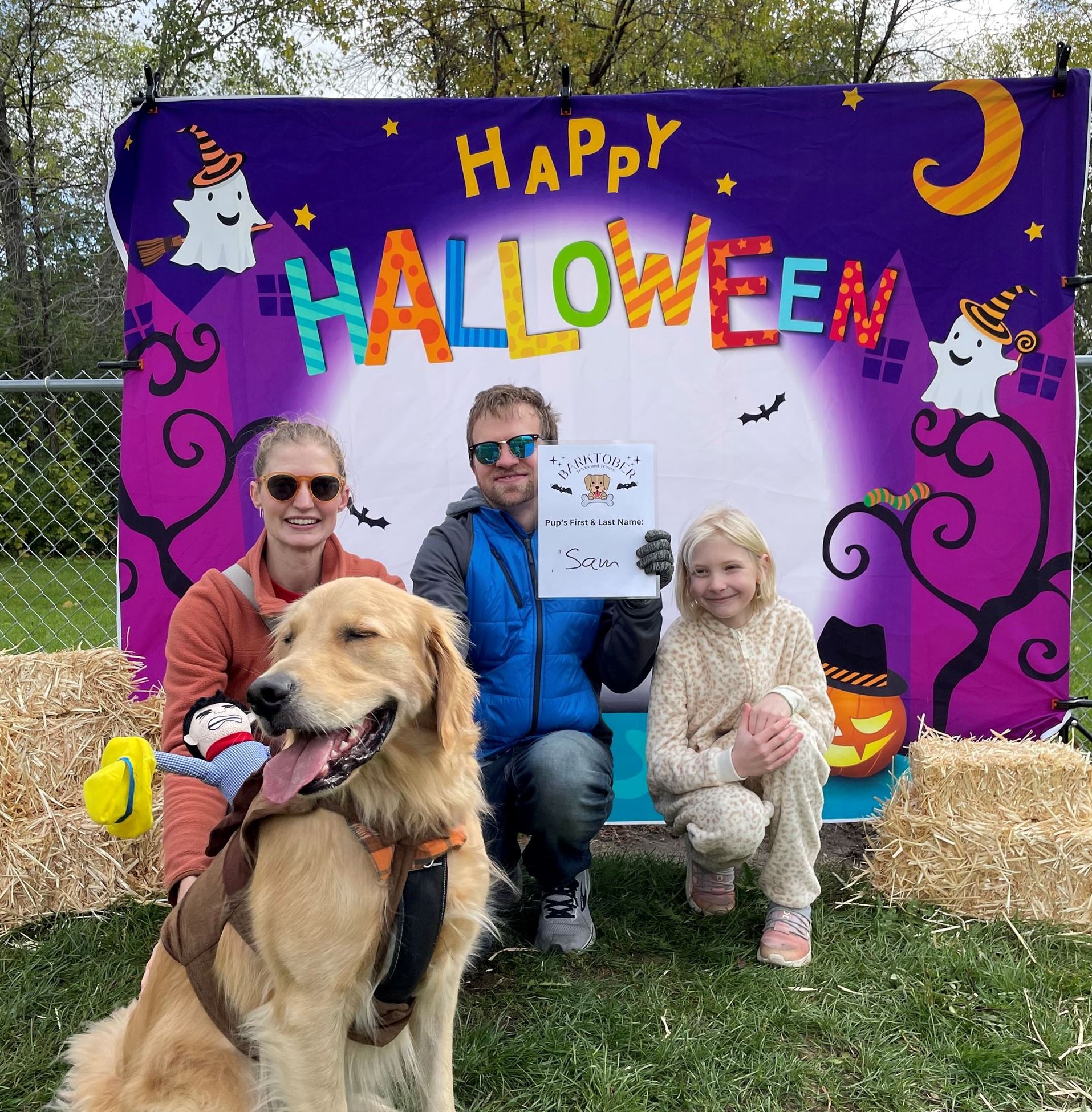 Two adults and one child poses with golden retriever dog wearing a cowboy costume.