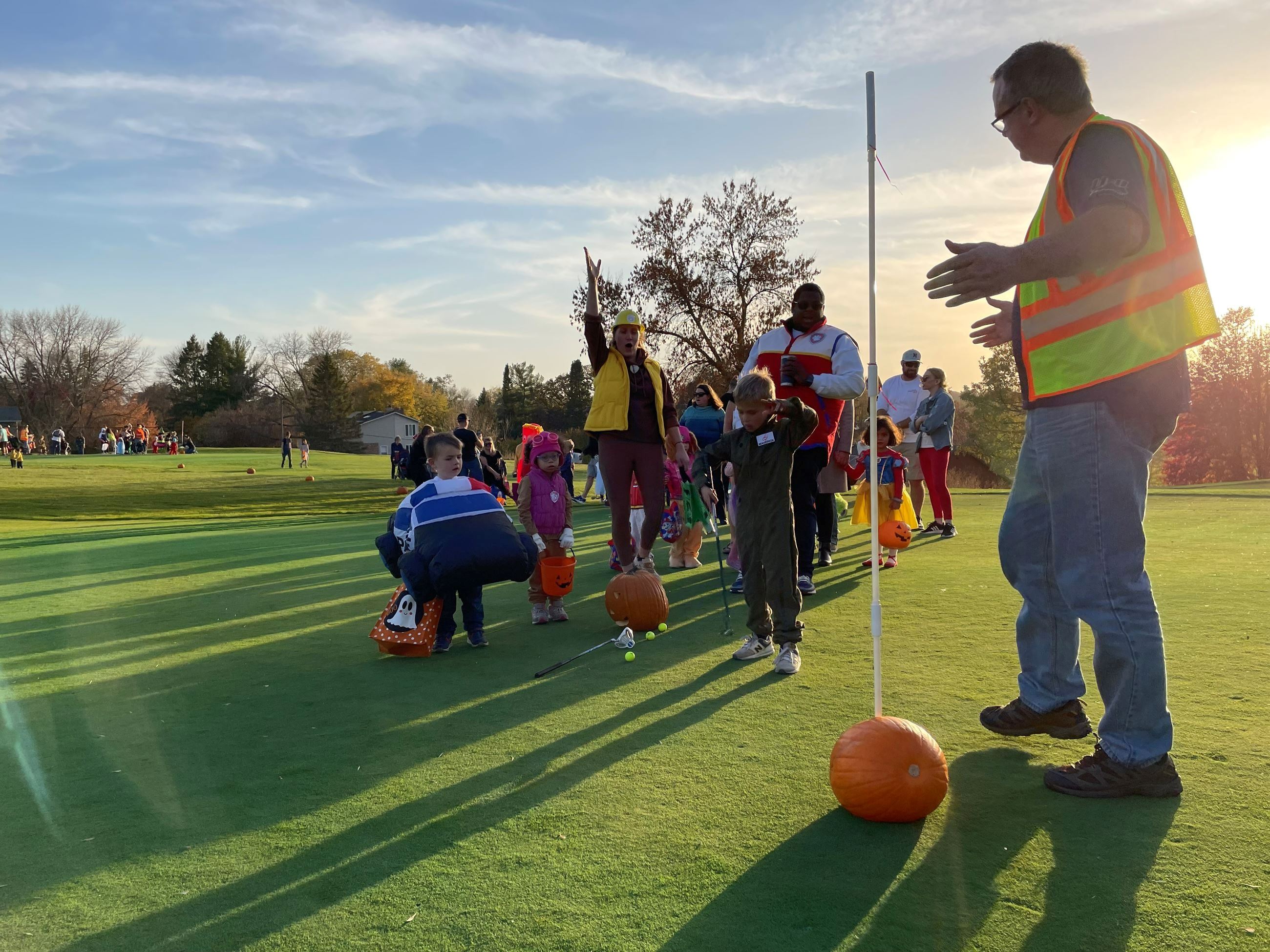 Man in yellow safety vest helping group of kids golf during trick or teeing event